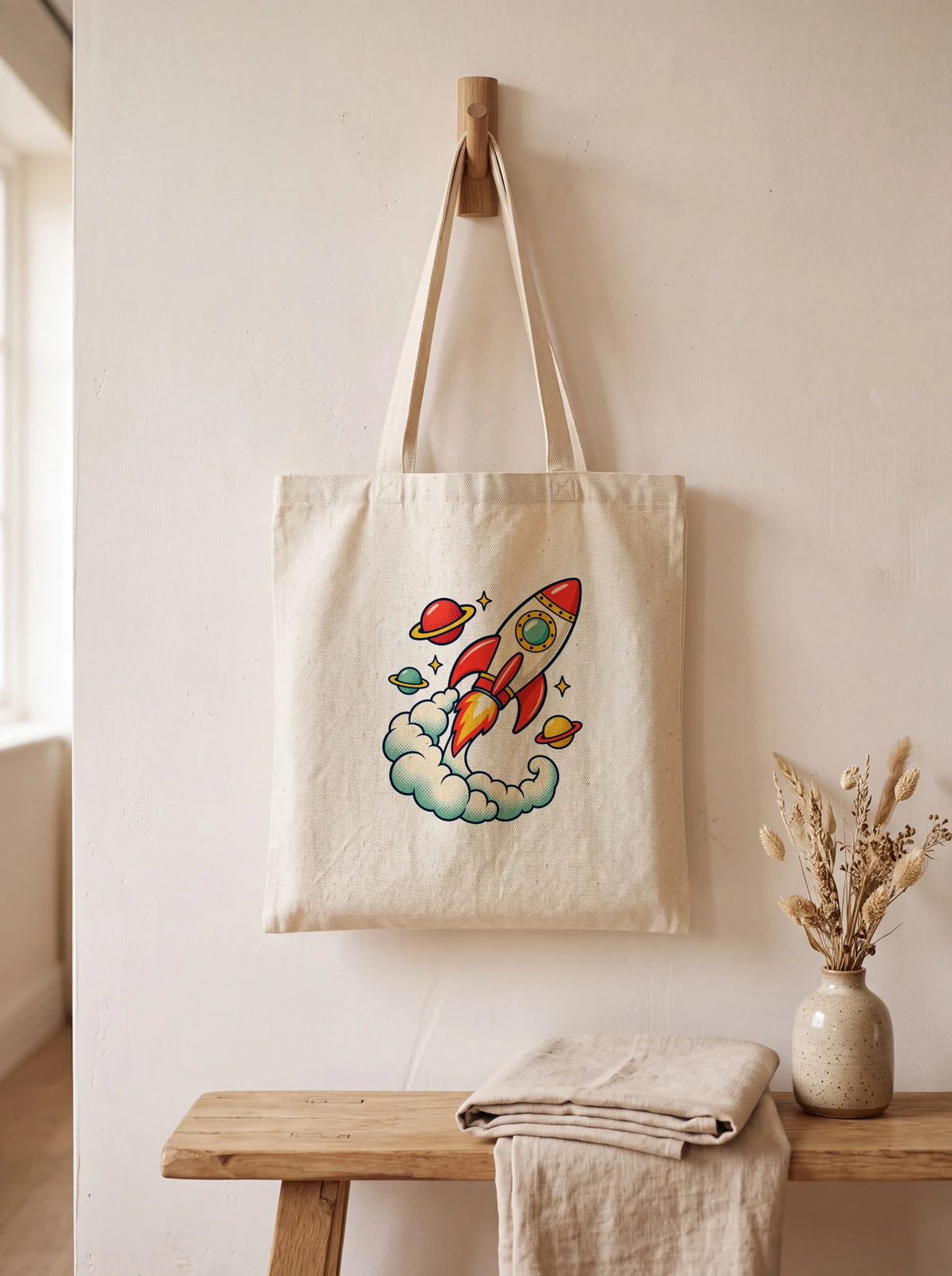 Natural canvas tote hanging from a wooden wall peg above a bench, rendered by SudoMock with the same rocket design on its front panel