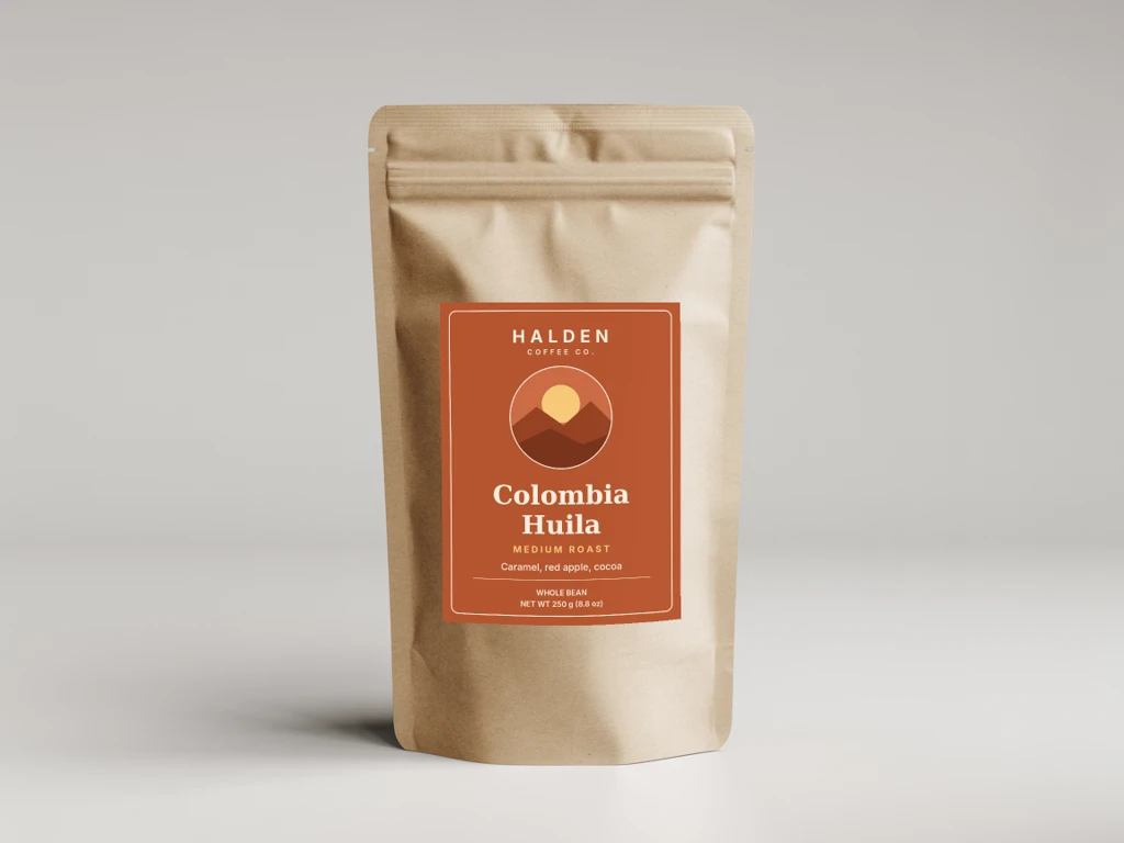 A kraft stand-up coffee pouch with a terracotta Colombia Huila medium roast label, rendered by API from one label file on the kraft pouch photo