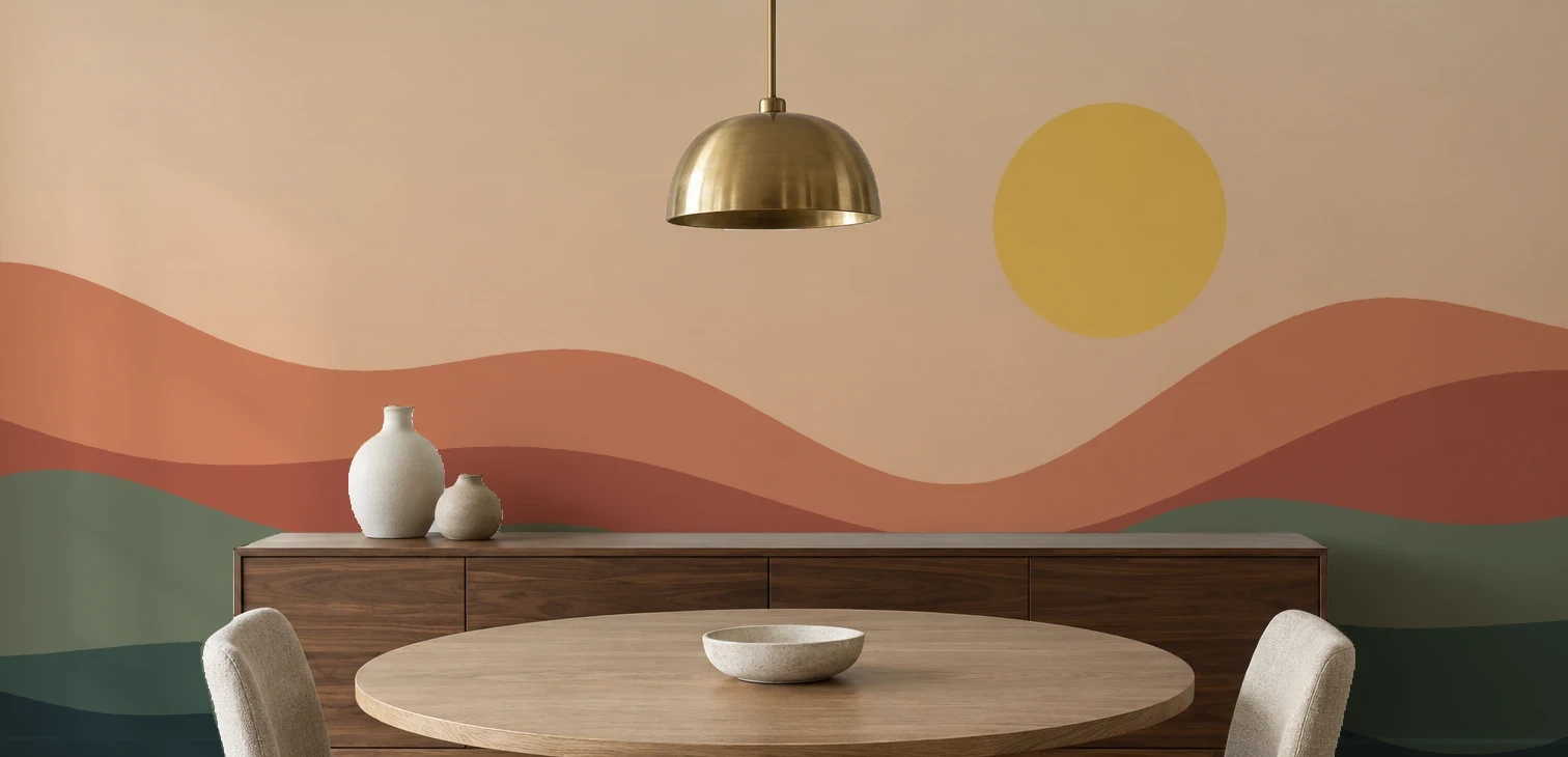 A flat sunset mural with a yellow sun and layered terracotta and green hills across a dining room wall, behind a walnut sideboard with two vases, a round table, two chairs and a brass pendant lamp